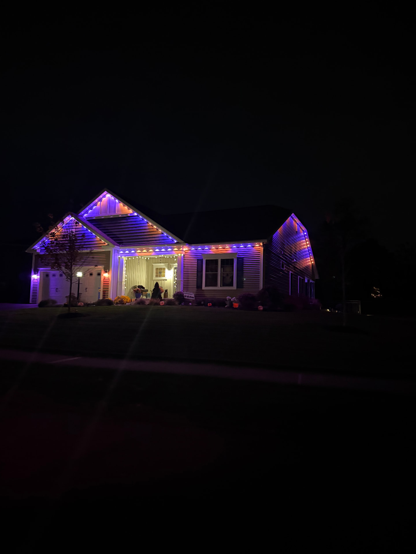 Street view of the same home at night with permanent lighting along the full roofline